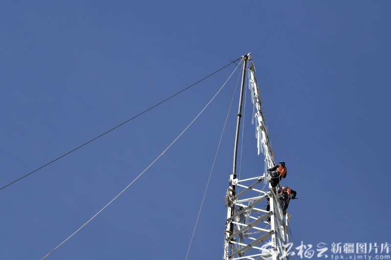5月9日，华能阿合奇县30万千瓦风电项目施工现场，工人在高空中搭建输电铁塔。