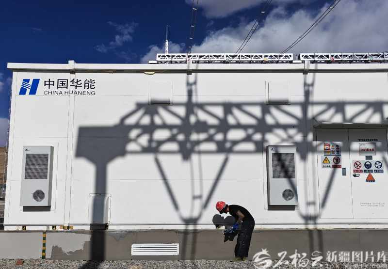 5月8日，华能阿合奇县30万千瓦风电项目升压汇集站，主变压器架构的影子投射在墙体上，一位工人正在维护墙面。