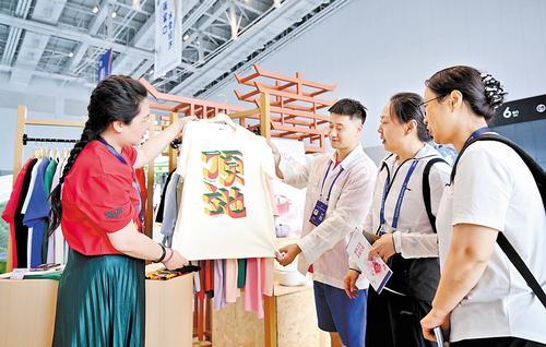 6月16日，在廊坊经洽会新业态新模式新场景消费展区，参展商（左）向观众介绍“顶天立地”成语文化衫。本报记者 赵永辉摄