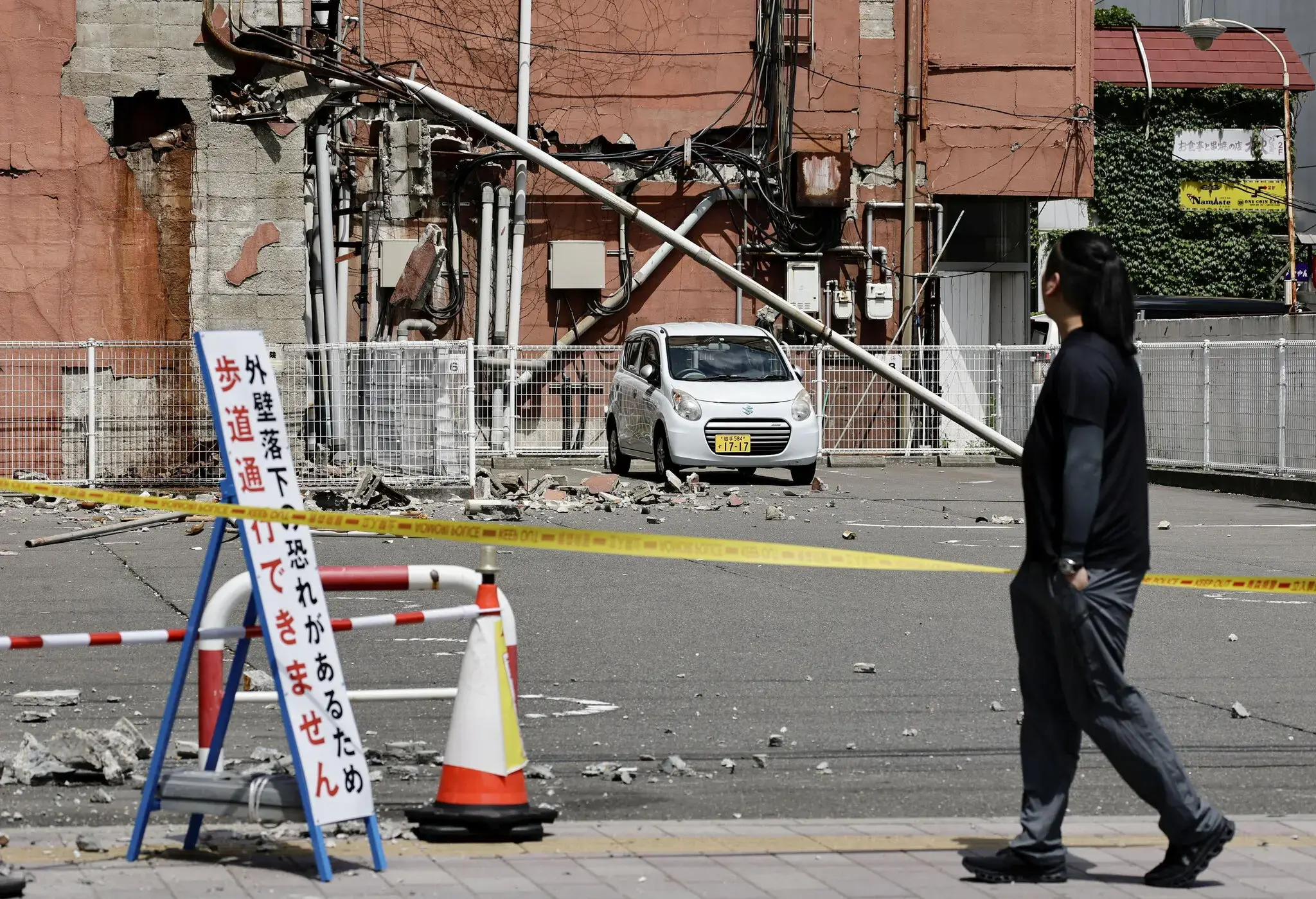 日本青森县八户市发生地震后，一名行人走过一栋建筑物的受损墙壁