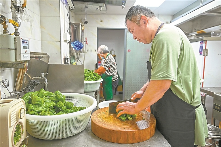 志愿者在厨房帮忙洗菜、切菜。