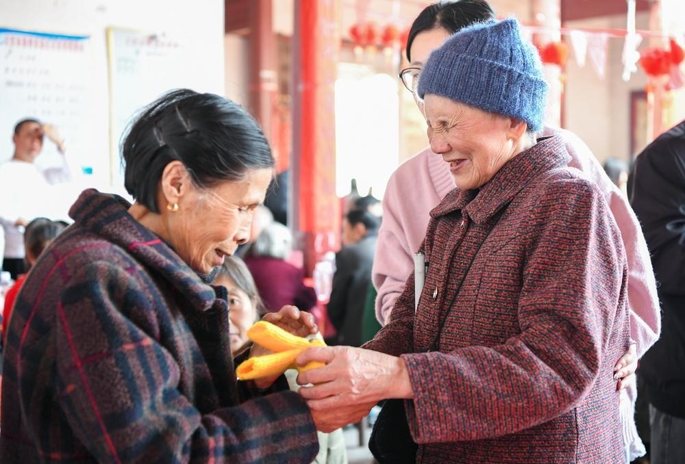 2025年铜鼓县高桥乡胆坑村的长寿宴上，刘孝英老人将亲手编织的手套送给百岁老人。