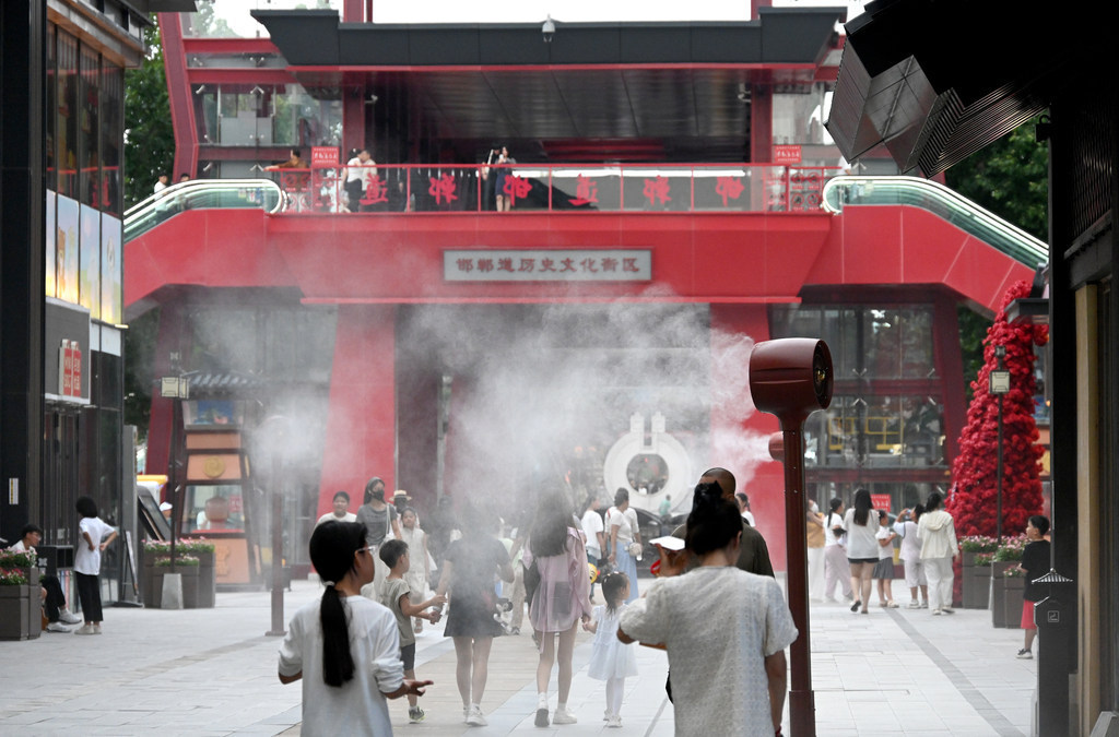 7月21日，在邯郸市邯郸道历史文化街区，游客从雾森风扇旁经过。