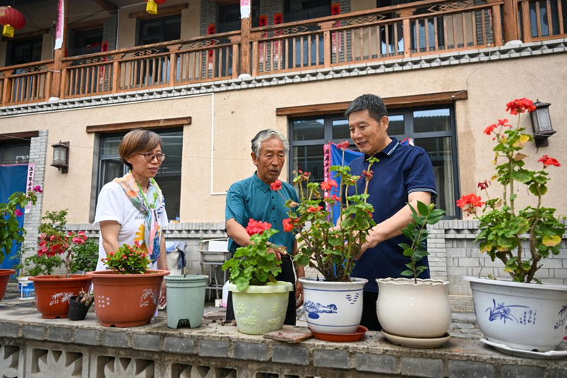 7月29日，村民孙振泽（中）在自家民宿向游客介绍自己的养花经验。