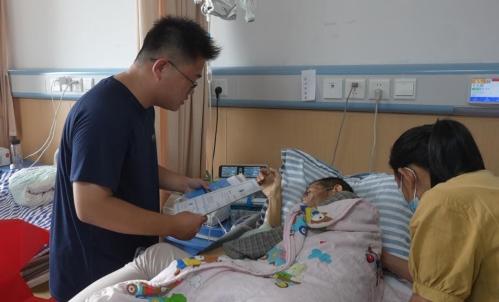 病床前，儿子朱锦林（左一）一字一句将录取通知书上的文字念给父亲听（图片来源南昌交通学院）