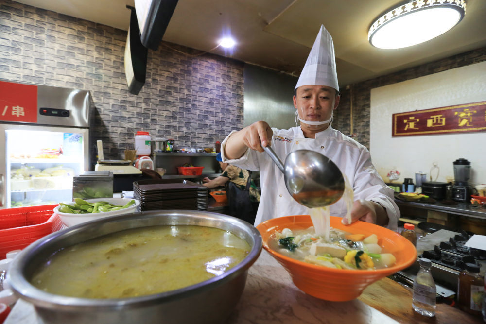 7月17日,甘肃省定西市安定区一家餐馆的厨师向麻辣烫中加浆水。新华社发(王克贤 摄)