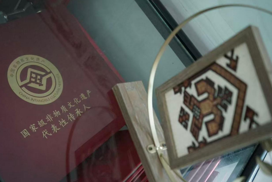 图为王瑞妹2018年获评第五批国家级非遗传承人时的认定证书，旁为其双面绣代表作。