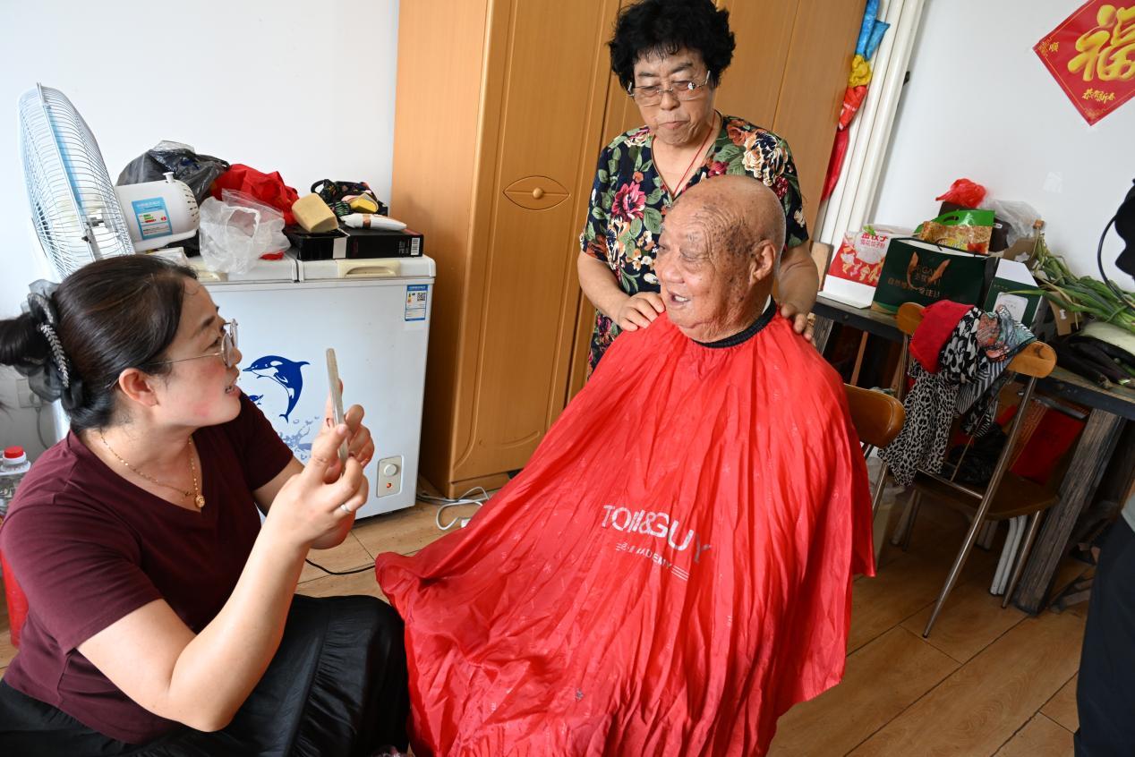 7月30日，王翠珍和儿媳妇解平利（左一）在给92岁的抗美援朝老兵王永昌理发。