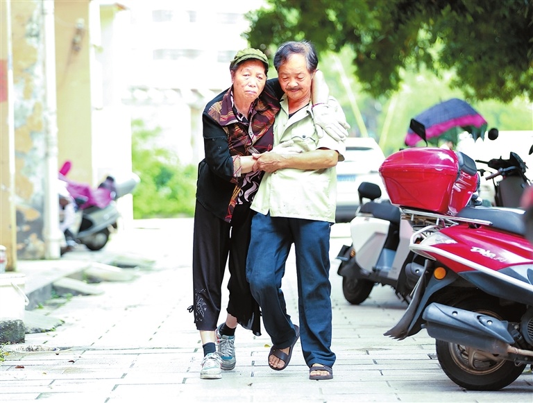 为防止肌肉萎缩、关节僵硬,李根金每天都要搀扶着妻子走路锻炼。