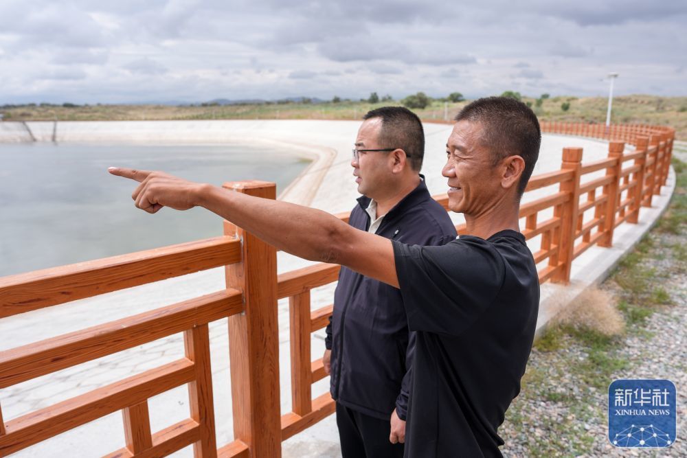 ↑8月11日，在古浪县八步沙林场，第三代治沙人郭玺（右）与当地水务部门工作人员观察蓄水池水位。