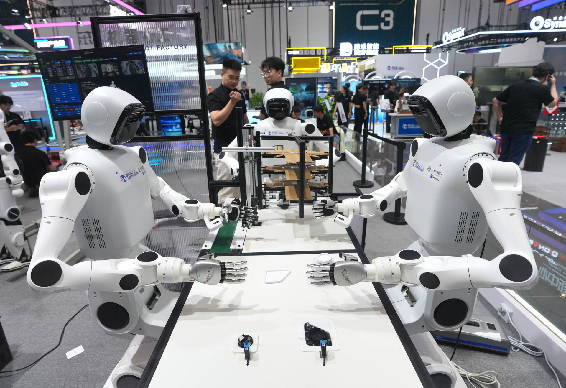 2026世界机器人大会,国地共建具身智能机器人创新中心(北京人形机器人创新中心)展位上,几台人形机器人正在操作台上协同工作。 (资料图)北京日报记者 和冠欣摄