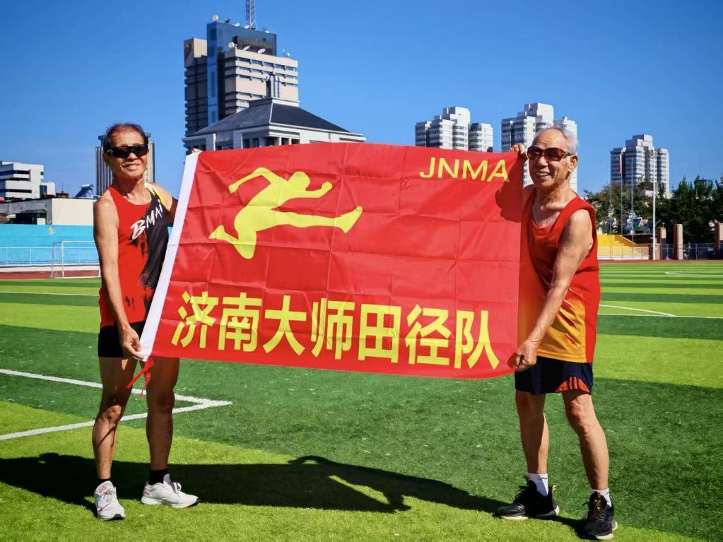 吕明璞(右)和队友一起展示济南大师田径队的队旗。
