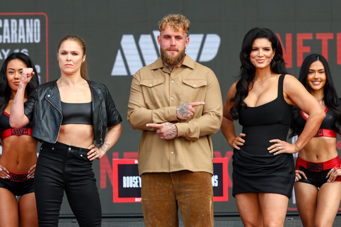 Ronda Rousey, Jake Paul, and Gina Carano posing on stage at an MMA press conference.