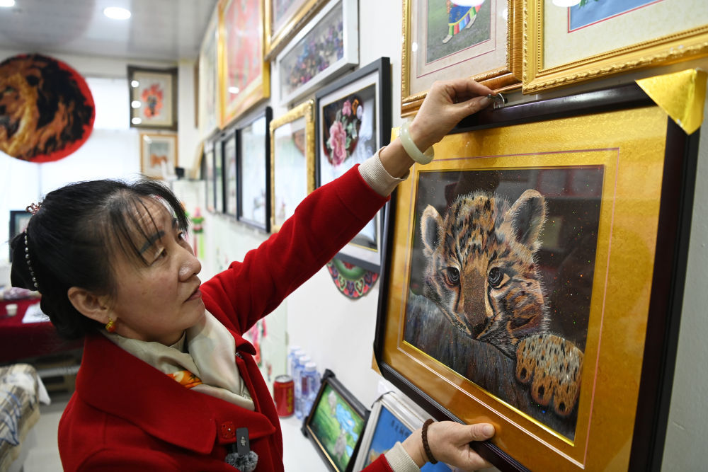 在天祝藏族自治县的自家店铺中，张才红将墩绣作品《雪豹》挂到墙面上。新华社记者　范培珅　摄