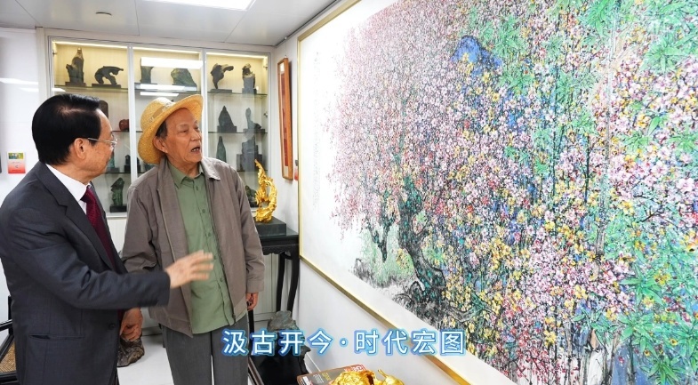 萧晖荣教授向万伯翱会长介绍其中国画《盛世繁华——十分春色》
