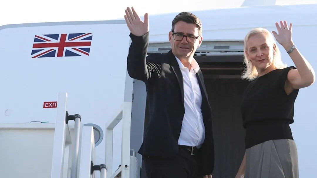 英国首相安迪·伯纳姆和玛丽-弗朗斯·范·希尔挥手登上飞机,机舱门旁可以看到英国国旗。