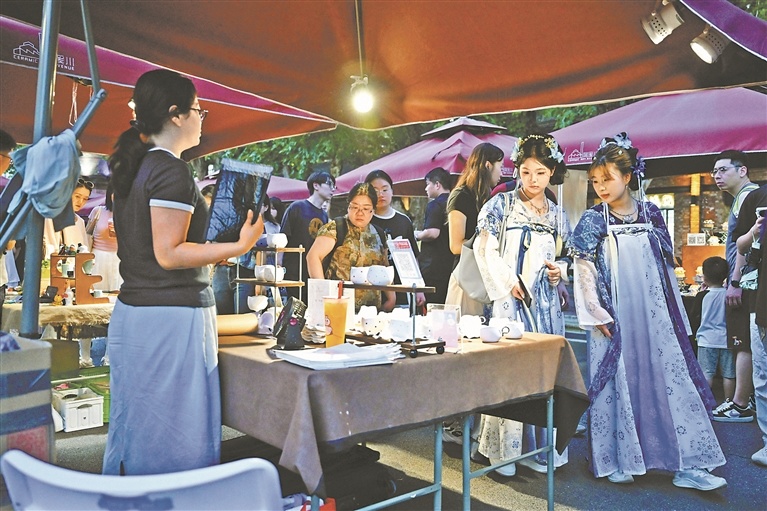7月25日,在景德镇陶溪川夜市,游客身着汉服,挑选创意瓷器。