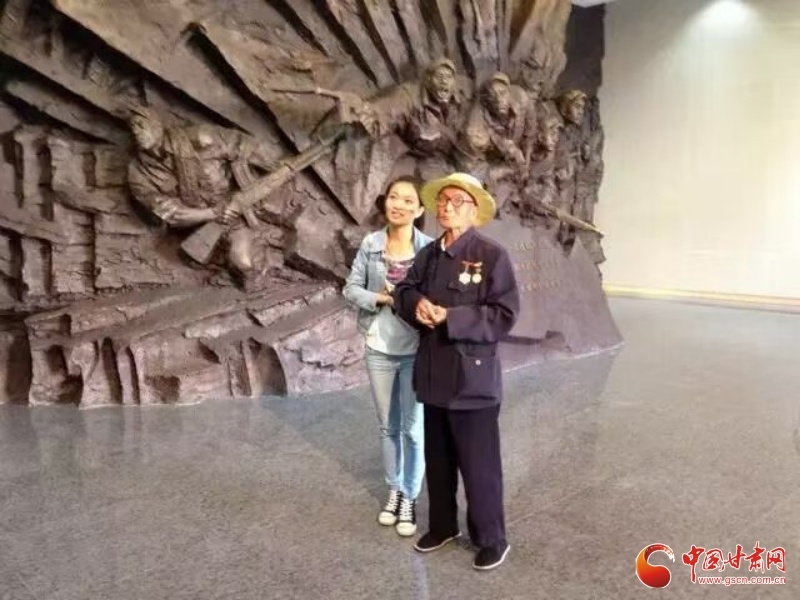 王丽娟搀扶着胡兴国驻足战役浮雕前,聆听老兵回忆战火岁月。