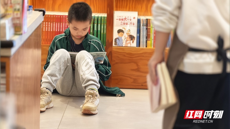 小男孩背靠书架席地而坐，捧书埋头，这个假期，书店的地板就是孩子最自在的小天地。