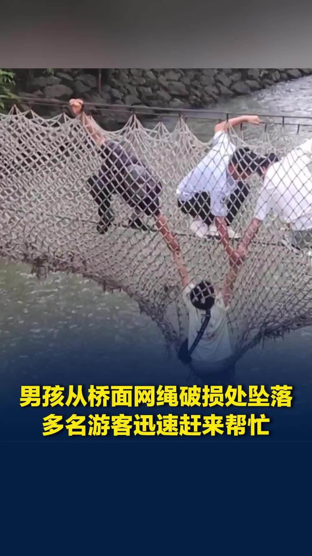 男孩从桥面网绳破损处坠落，双手紧紧抓住网绳，悬在半空，多名游客迅速赶来帮忙