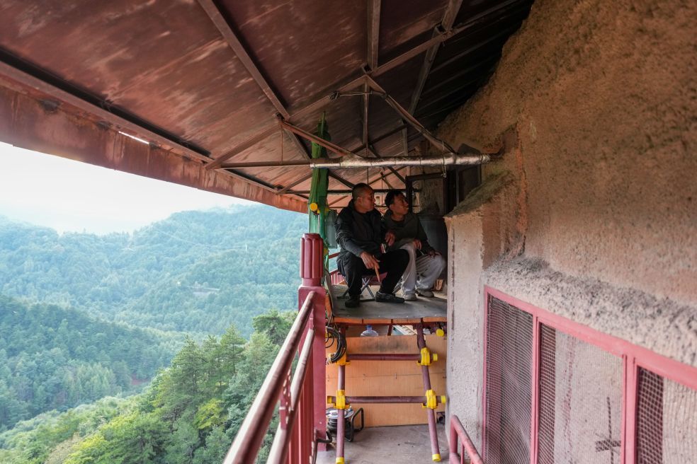 9月22日,在麦积山石窟第157窟前的“工位”上,麦积山石窟艺术研究所保护研究室高级文物修复师牟常有(左)向徒弟杨志强传授传统塑像修复技艺。新华社记者 郎兵兵 摄