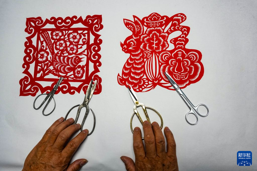 10月16日,王新胜展示母亲用过的剪刀、剪纸作品(左)与自己使用的剪刀、剪纸作品(右)。新华社记者 郎兵兵 摄
